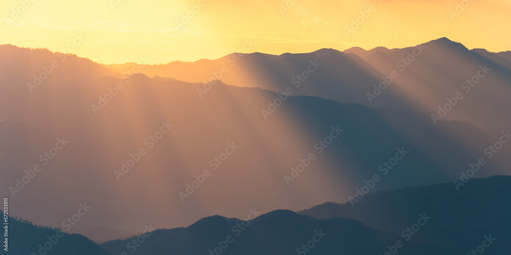 Panoramic scene of sunlight shining through the mountain range at sunset.