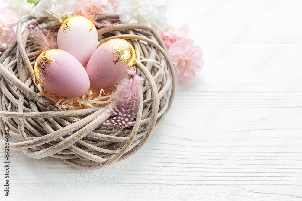 Easter eggs painted pink and gold and feathers in a nest on a white wooden background. Easter eggs painted pink and gold and feathers in a nest on a white wooden background.