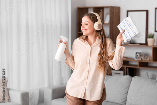 Fotobehang Young woman in headphones with rag and detergent dancing at home