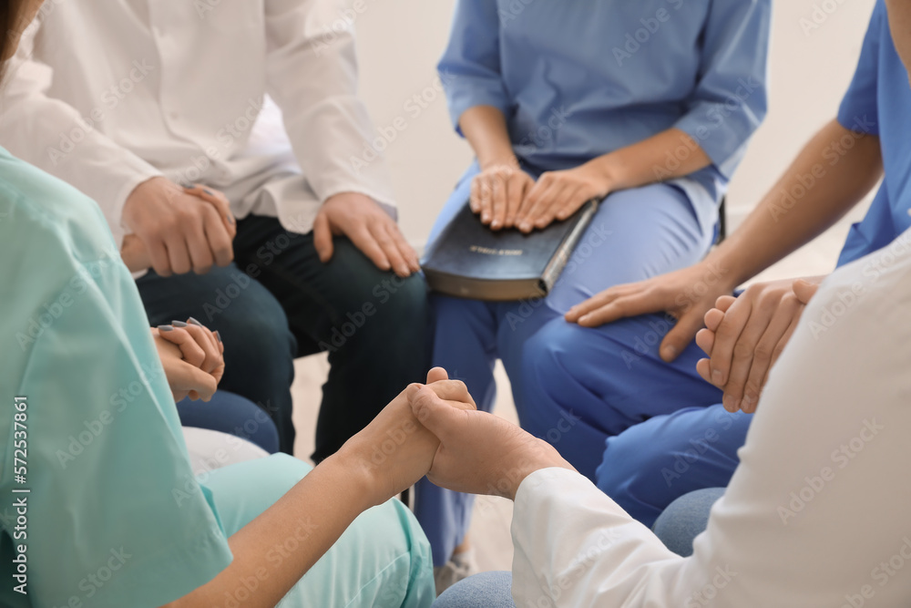 Fototapeta premium Group of doctors praying with Holy Bible in clinic, closeup