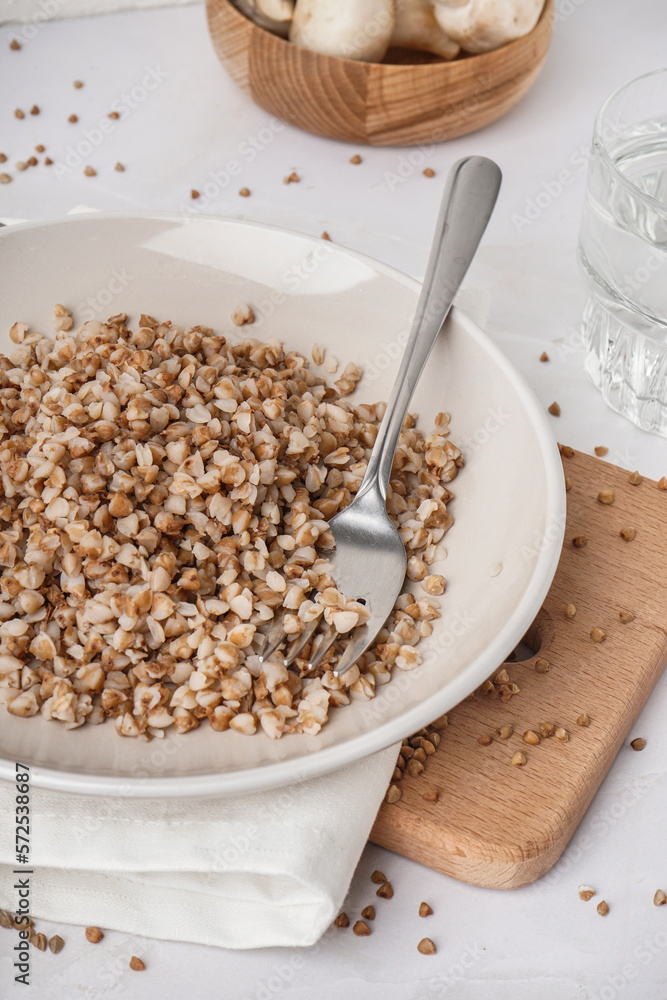 Board with plate of tasty buckwheat porridge on white table Board with plate of tasty buckwheat porridge on white table