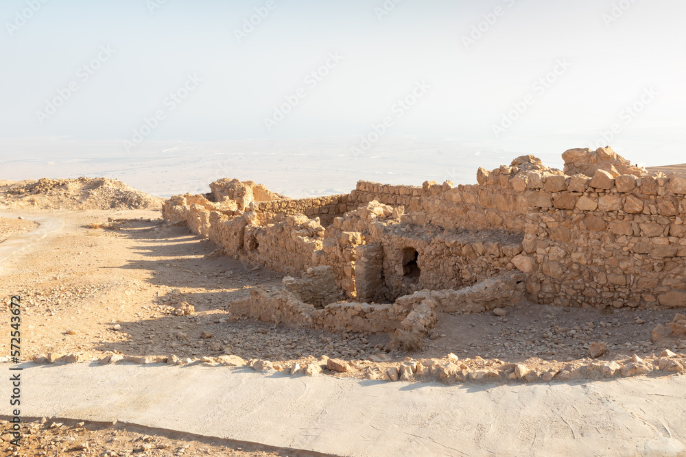 Fototapeta premium The remains of internal buildings in the rays of the rising sun in the ruins of the fortress of Masada - is a fortress built by Herod the Great on a cliff-top off the coast of the Dead Sea, Israel