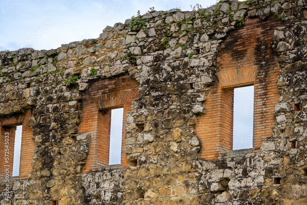 Old stone wall ruin with 3 windows partially destroyed and restored with orange bricks. 