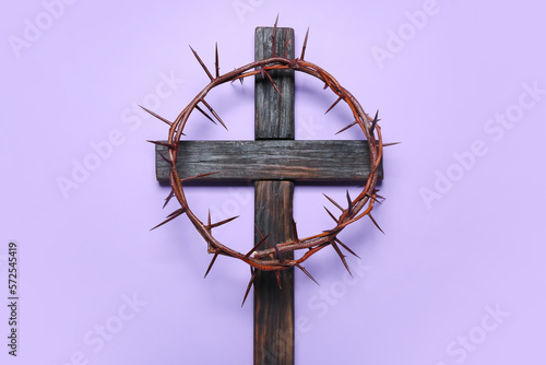 Wooden cross with crown of thorns on lilac background. Good Friday concept