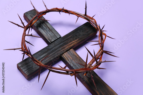 Wooden cross with crown of thorns on lilac background  closeup. Good Friday concept