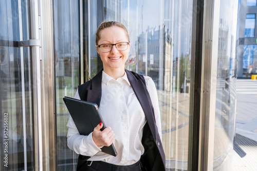 Portrait of successful business woman in stylish suit using laptop posing next to city office building. Confident female CEO smiling. Successful Diverse Business Manager.