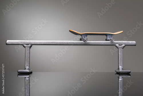 Children's fingerboard on a metal railing on a gray gradient background, a small skateboard