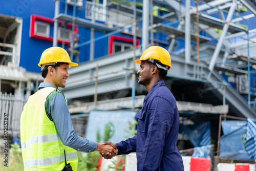 African American Technician, Asian Engineer doing handshake together. Group of Multi-Ethnic Blue-collar worker. Teamwork of Architect review plans at construction site.
