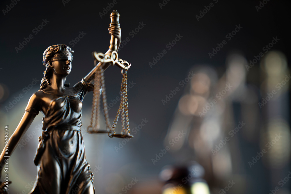 Law and justice concept. War crimes. Gavel and Themis sculpture in lawyers office. Gray bokeh background.