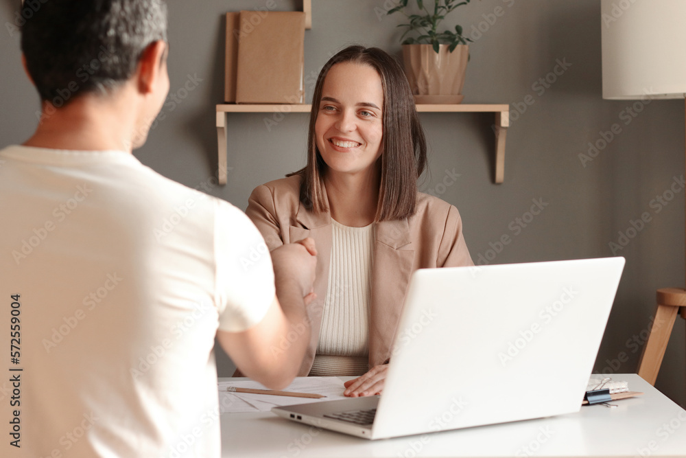 Indoor shot of business people shaking hands after meeting, sitting at table in office, being ready to sign contract, smiling happily, woman and man working together. Indoor shot of business people shaking hands after meeting, sitting at table in office, being ready to sign contract, smiling happily, woman and man working together.