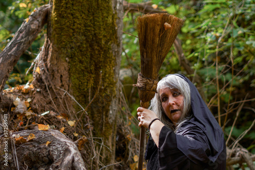 witch with tousled white hair and broom in the forest