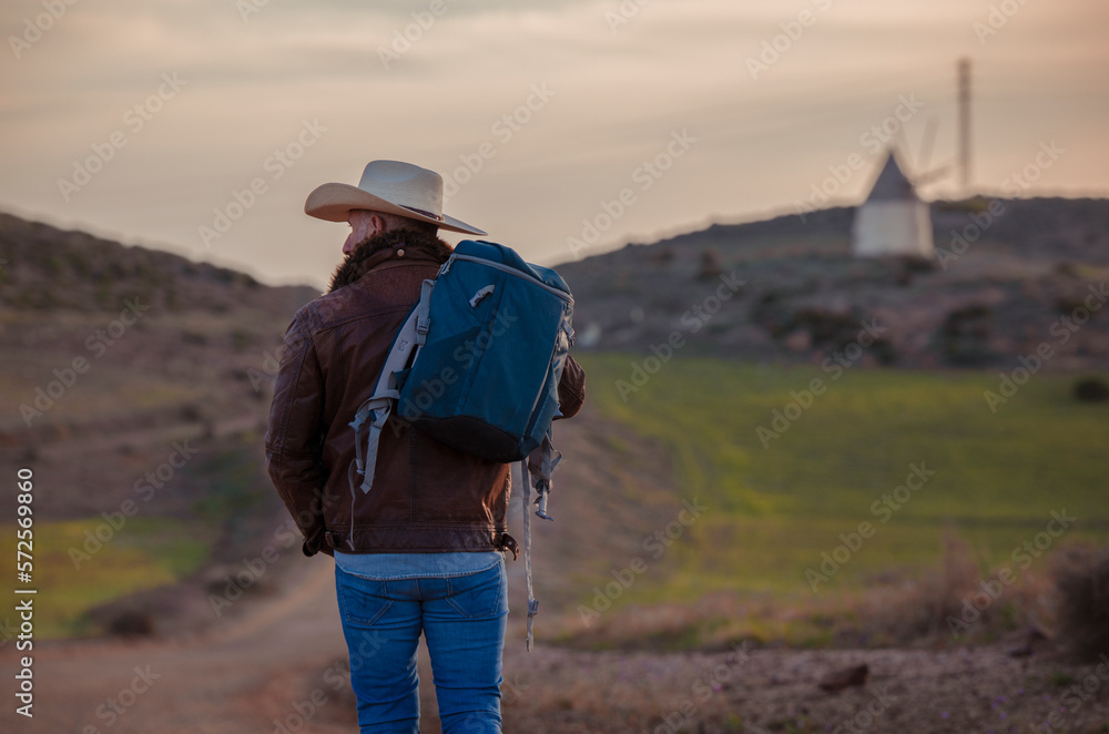 Adult man in cowboy hat walking on dirt road against sky during sunrise