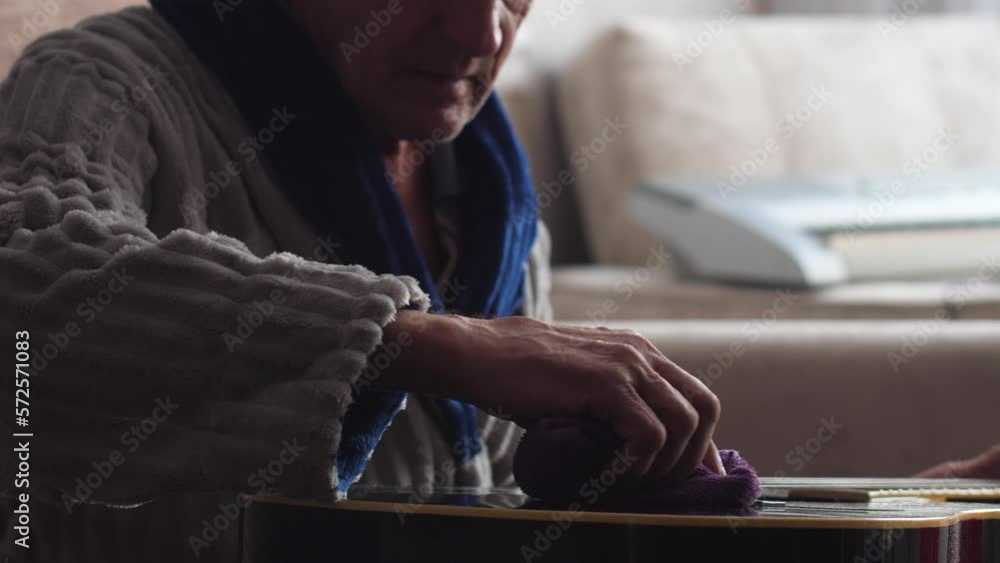 a caucasian pensioner wipes an acoustic guitar from dust with a rag while at home. an old man's hobby is playing the guitar. retired home life. real people, passion for music a caucasian pensioner wipes an acoustic guitar from dust with a rag while at home. an old man's hobby is playing the guitar. retired home life. real people, passion for music