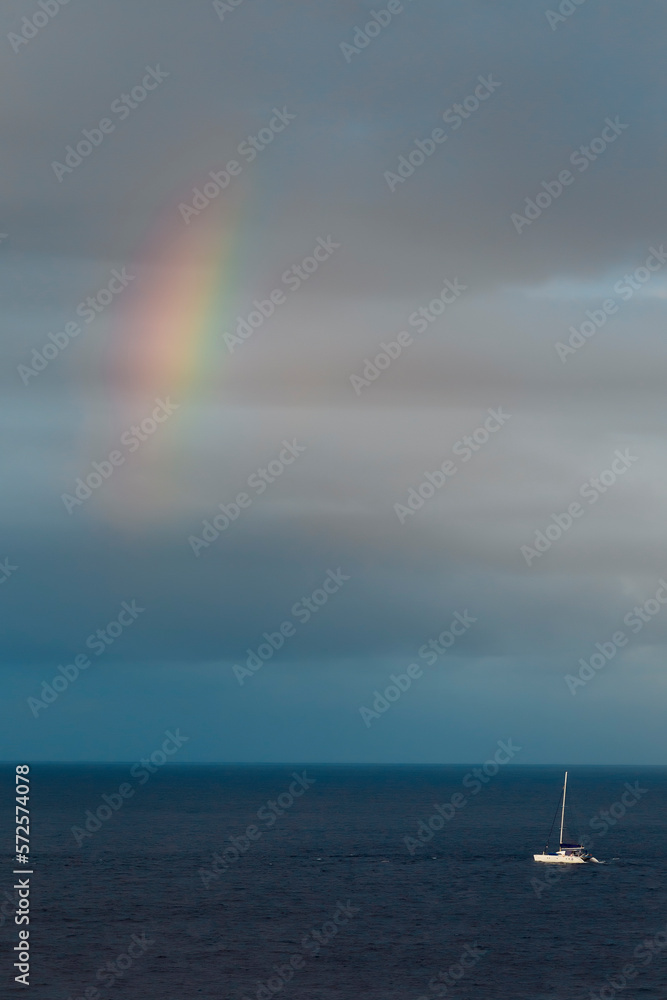 Rainbow on cloudy sky over sailboat drifting on calm sea waters, Bali, Indonesia Rainbow on cloudy sky over sailboat drifting on calm sea waters, Bali, Indonesia