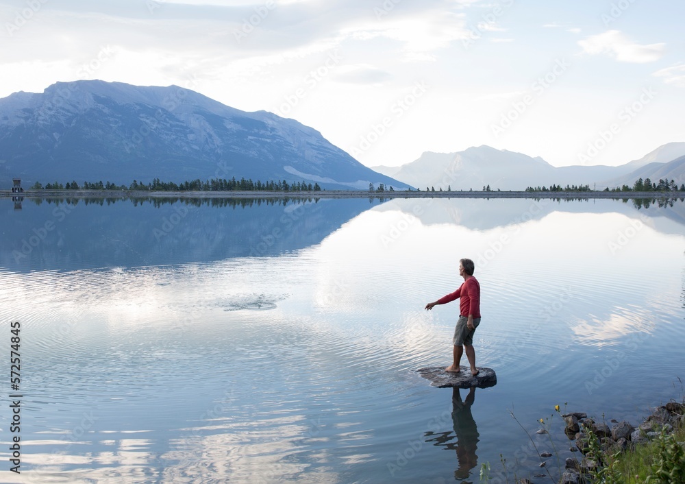 Man skips rock from island, mountains distant Man skips rock from island, mountains distant