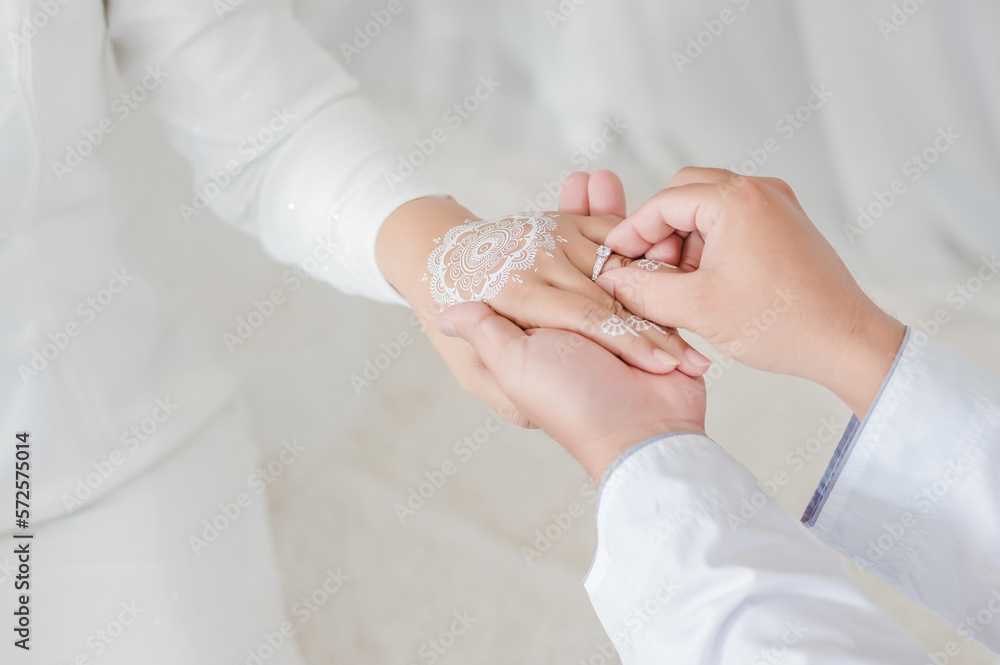 malay wedding groom bolstering ring on bride's finger. Groom wear