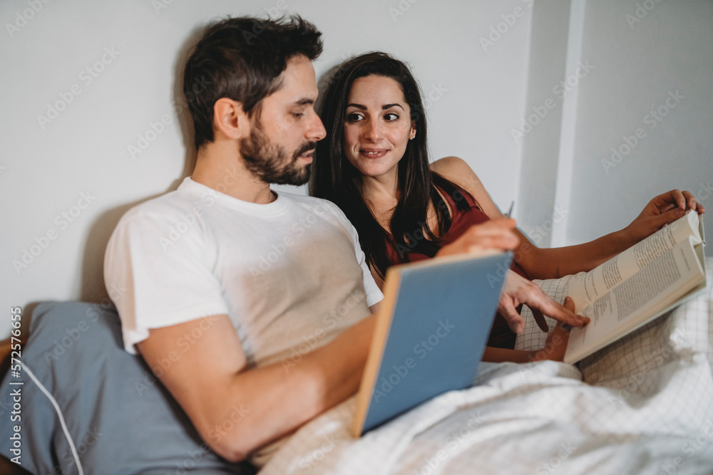 Loving couple reading under covers in bed at home in a moment of rest Loving couple reading under covers in bed at home in a moment of rest