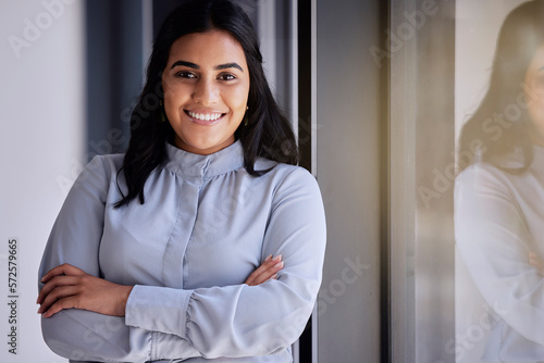 Portrait, window and vision with a business woman in the office, standing arms crossed for growth. Mission, motivation and smile with a happy female employee at work for corporate company success