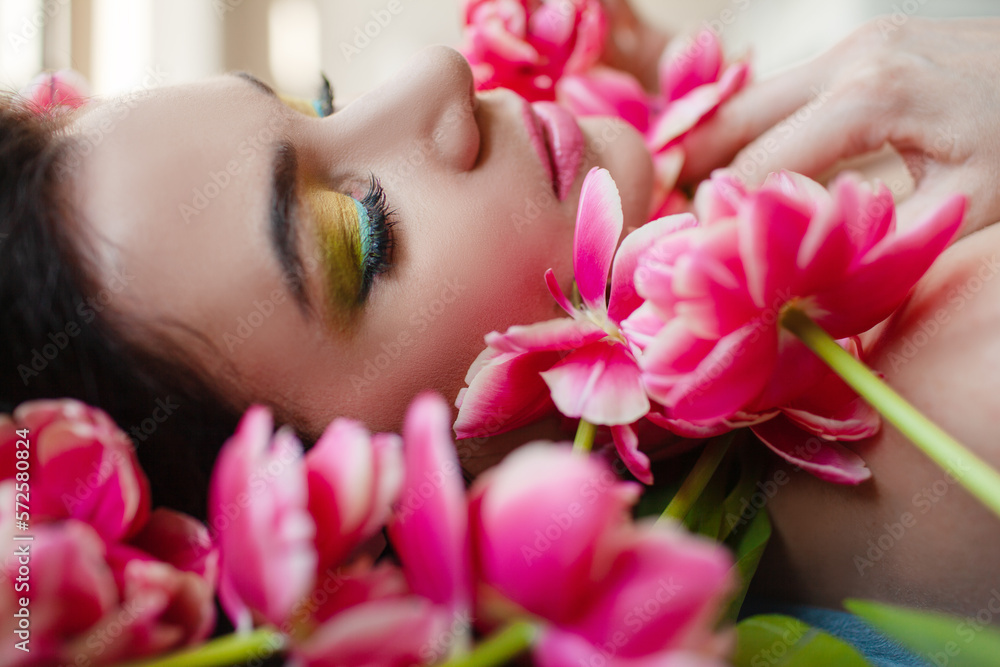 The face of beautiful woman with colorful make-up and flowers . The attractive woman lies in tulips. The face of beautiful woman with colorful make-up and flowers . The attractive woman lies in tulips.