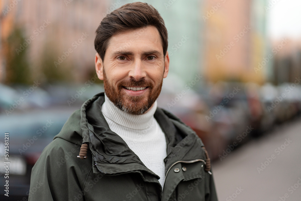 Confident, handsome man with a beard stands smiling on a city street. A young man on the background of the city. Confident, handsome man with a beard stands smiling on a city street. A young man on the background of the city.