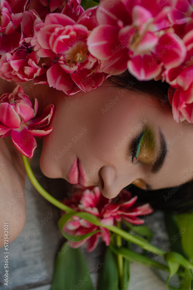 The face of beautiful woman with colorful make-up and flowers . The attractive woman lies in tulips. The face of beautiful woman with colorful make-up and flowers . The attractive woman lies in tulips.