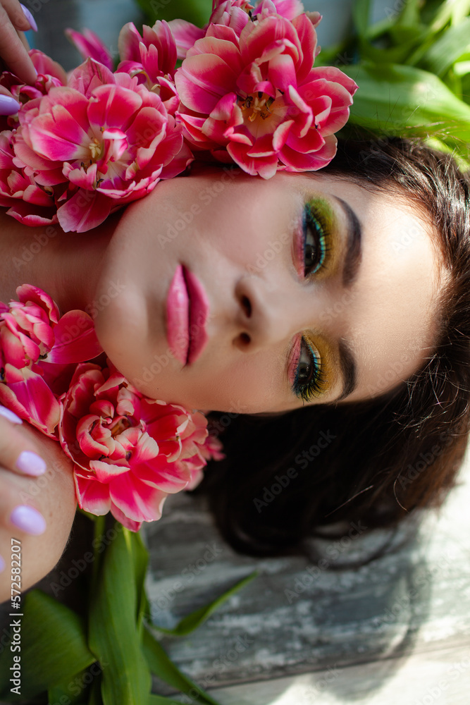 The face of beautiful woman with colorful make-up and flowers . The attractive woman lies in tulips. The face of beautiful woman with colorful make-up and flowers . The attractive woman lies in tulips.