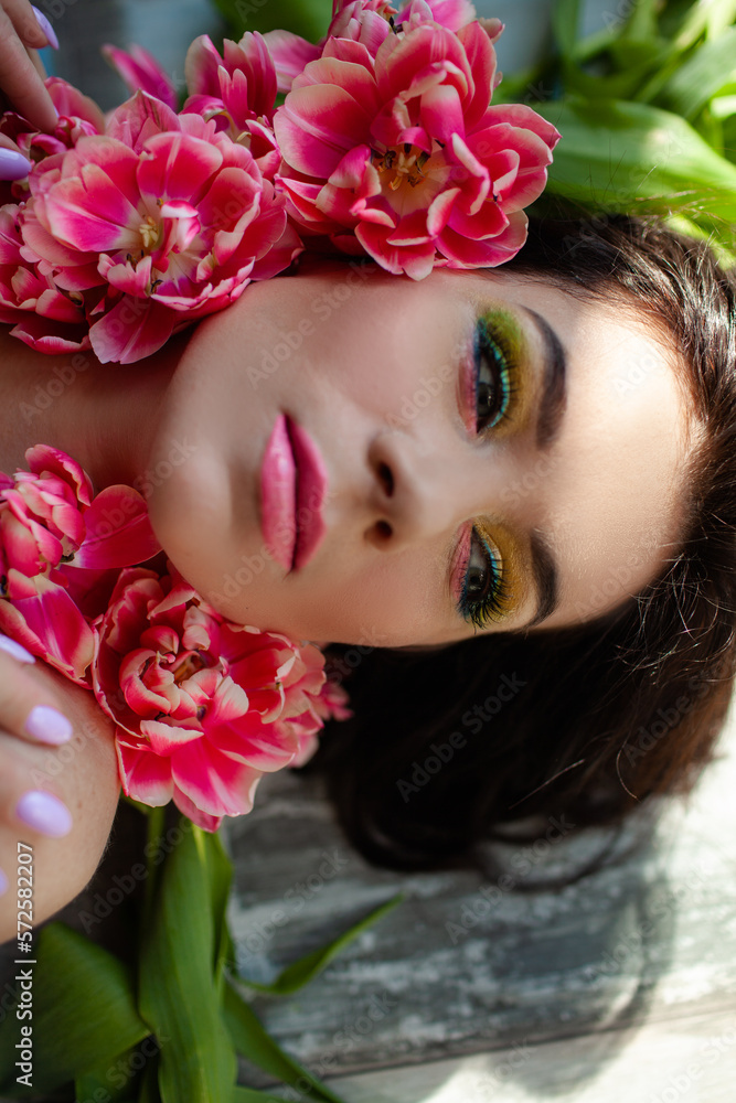 The face of beautiful woman with colorful make-up and flowers . The attractive woman lies in tulips.