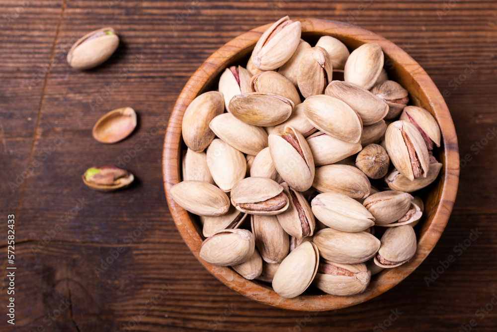 Top view, on an old wooden background, extreme close-up, a bowl with pistachios in shell.