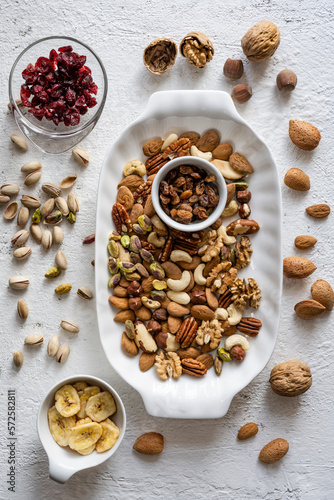 Top view, close-up, on a textured white concrete background, some bowls and a tray with mixed dried and dehydrated fruits