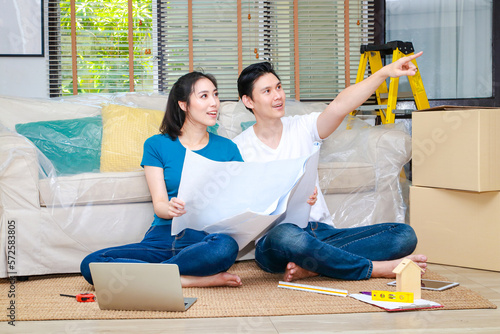 Asian couple renovating their home to be beautiful and livable Sit on the floor of the room looking at the house interior construction drawings. real estate concept residence. moving house