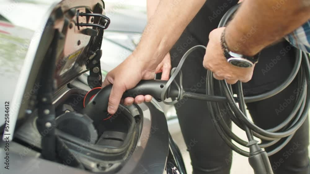 The hands of a man connecting one end of a cable to the battery of an electric car. Slow motion handheld closeup shot.
The hands of a man connecting one end of a cable to the battery of an electric car. Slow motion handheld closeup shot.