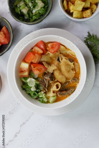 Indonesian traditional food named "soto betawi beef and coconut milk sauce" i.e. beef soup from Betawi Jakarta. Served on bowl isolated on garnish background blurred