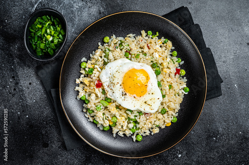 Fried rice with chicken, egg and vegetables in a plate. Black background. Top view