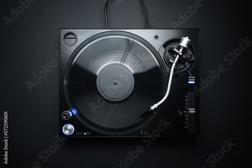 Flat lay photo of DJ turntable playing vinyl record on black background. Professional analog record player shot directly from above