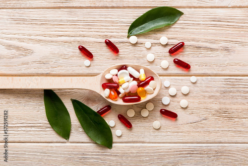 Vitamin capsules in a spoon on a colored background. Pills served as a healthy meal. Red soft gel vitamin supplement capsules on spoon