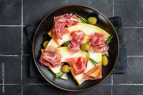 Prosciutto ham and melon salad in a plate. Black background. Top view