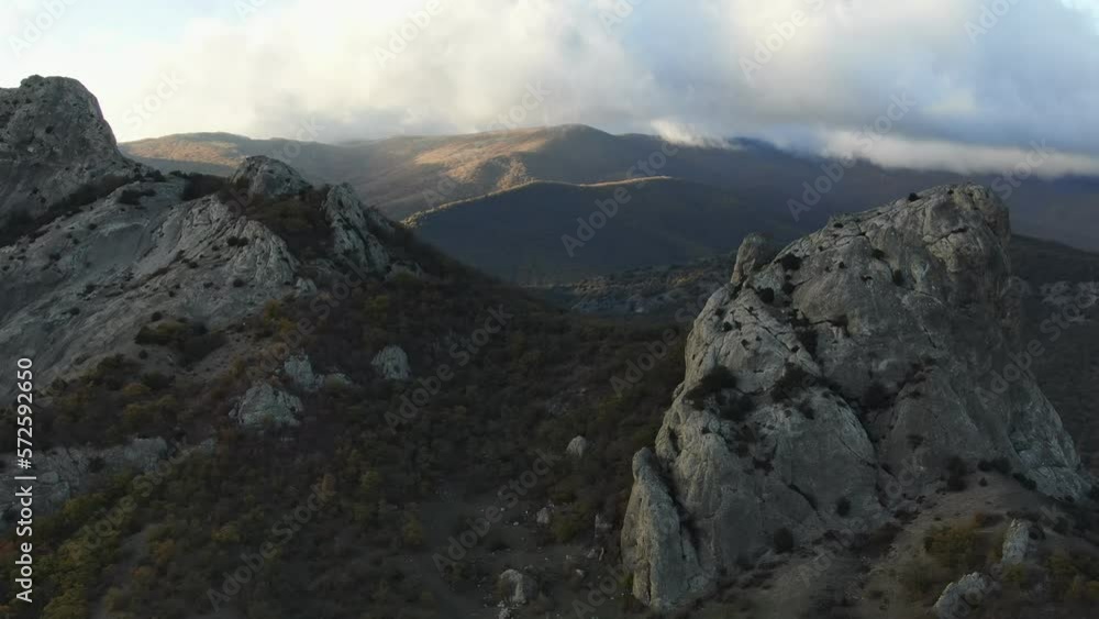 Aerial view of the autumn sunset in the mountains when the clouds crawl over the tops of the mountains and the rays flood the slopes overgrown with forest. Crowns of trees of different shades of green