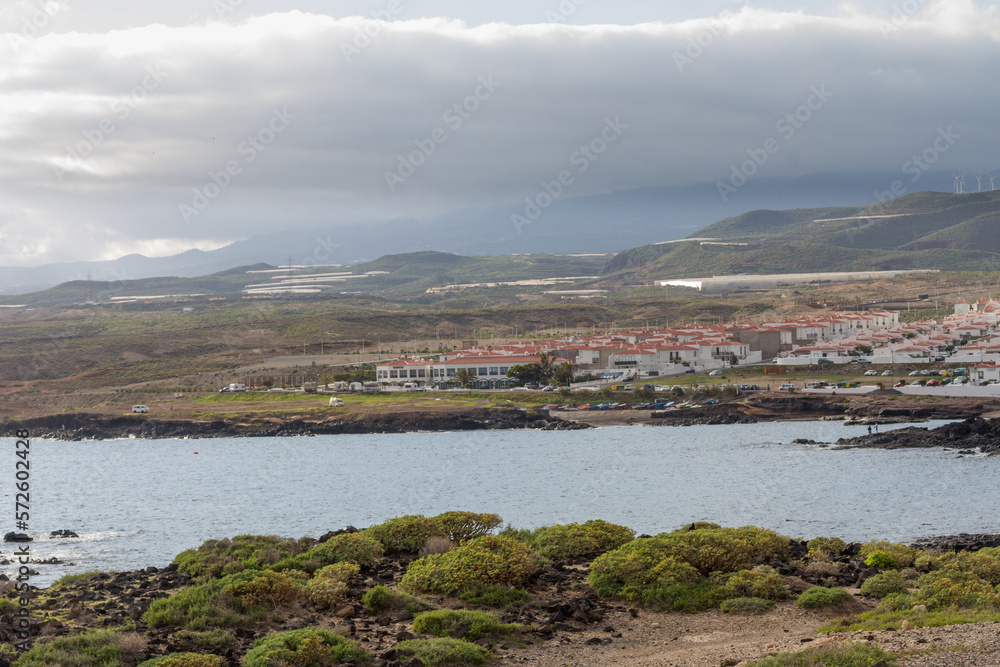 Crystal clear water bay with typical Canarian town in the background with mountains and storm clouds. Tenerife, Canary Islands. Spain