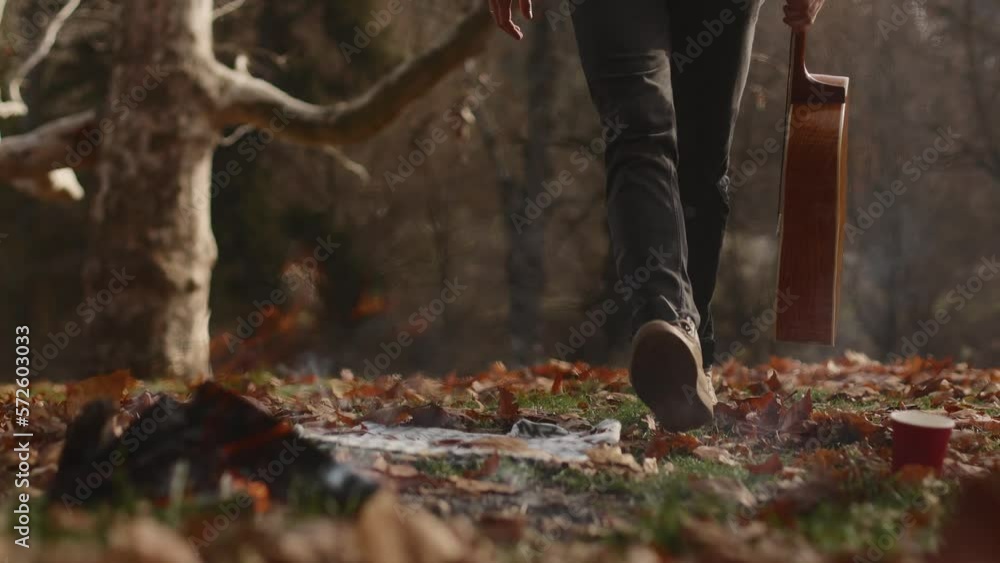 A young man, a boy, a traveler, approaches the fire in the meadow of the autumn forest, sits down on the ground and plays the guitar. Relaxing in nature alone. High quality 4k footage A young man, a boy, a traveler, approaches the fire in the meadow of the autumn forest, sits down on the ground and plays the guitar. Relaxing in nature alone. High quality 4k footage