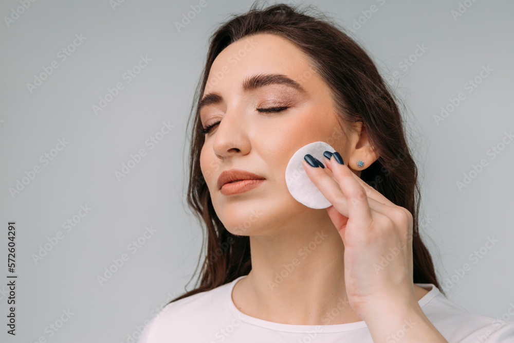 young dark-haired girl removes makeup from her face with a cotton pad young dark-haired girl removes makeup from her face with a cotton pad