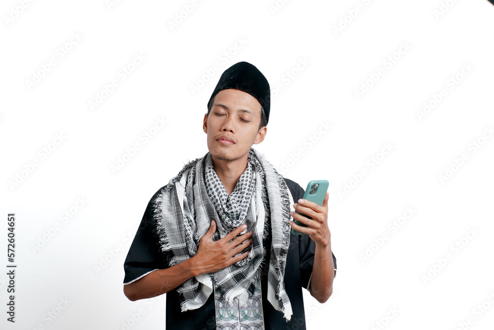 Religious muslim asian man wearing turban, muslim dress and cap. Holding a smartphone while holding the chest. isolated on white background. Religious muslim asian man wearing turban, muslim dress and cap. Holding a smartphone while holding the chest. isolated on white background.