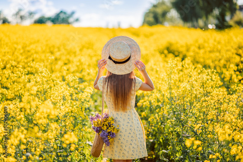 girl in a hat in a field of yellow flowers, rear view