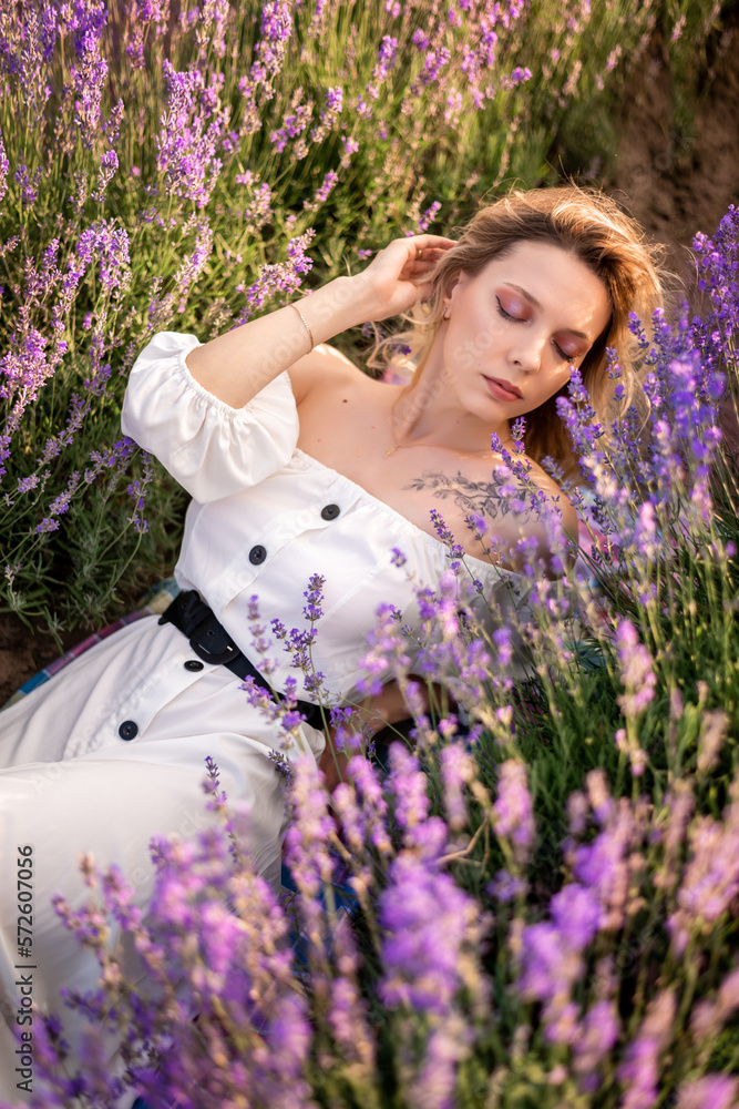 young blonde woman in a white dress lies in lavender flowers. Top view , portrait young blonde woman in a white dress lies in lavender flowers. Top view , portrait