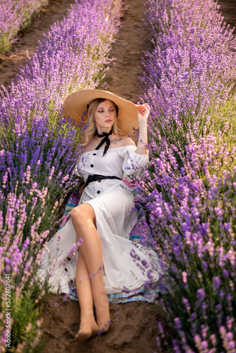 young woman in a white dress and a big hat is lying in lavender flowers. A field in Provence