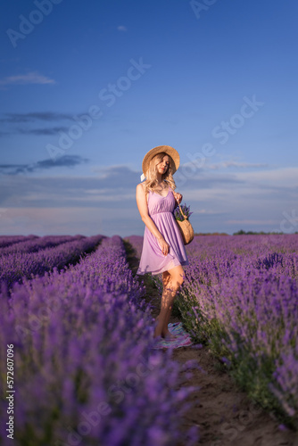 beautiful young woman in a hat and a short lilac dress stands in a field of lavender
