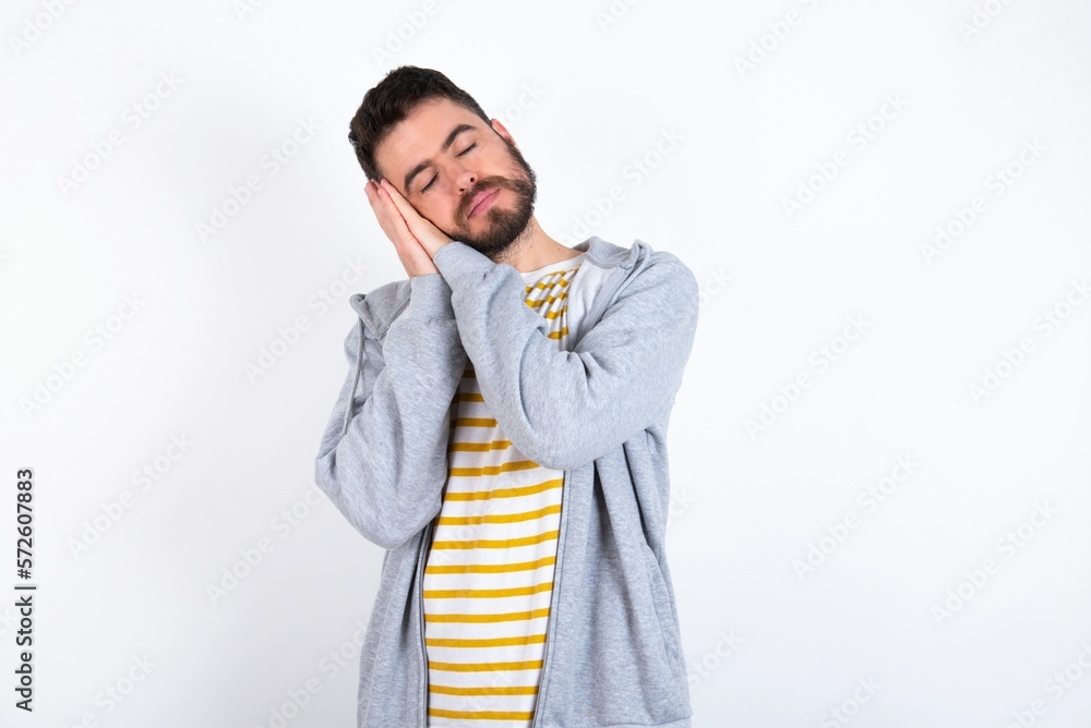 caucasian man wearing casual sportswear over white wall sleeping tired dreaming and posing with hands together while smiling with closed eyes. caucasian man wearing casual sportswear over white wall sleeping tired dreaming and posing with hands together while smiling with closed eyes.