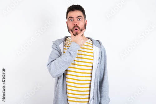 caucasian man wearing casual sportswear over white wall Looking fascinated with disbelief, surprise and amazed expression with hands on chin