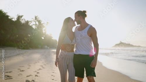 Young biracial happy couple and walking on the beach together enjoying summer front shot. Cheerful boyfriend and girlfriend relaxing and taking a walk at the seaside hugging and kissing at sunrise.