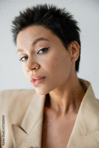 portrait of trendy woman with short brunette hair and makeup looking at camera isolated on grey.