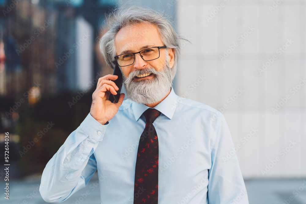 Portrait of senior businessman in light blue shirt with red tie talking on the phone outside smiling Portrait of senior businessman in light blue shirt with red tie talking on the phone outside smiling